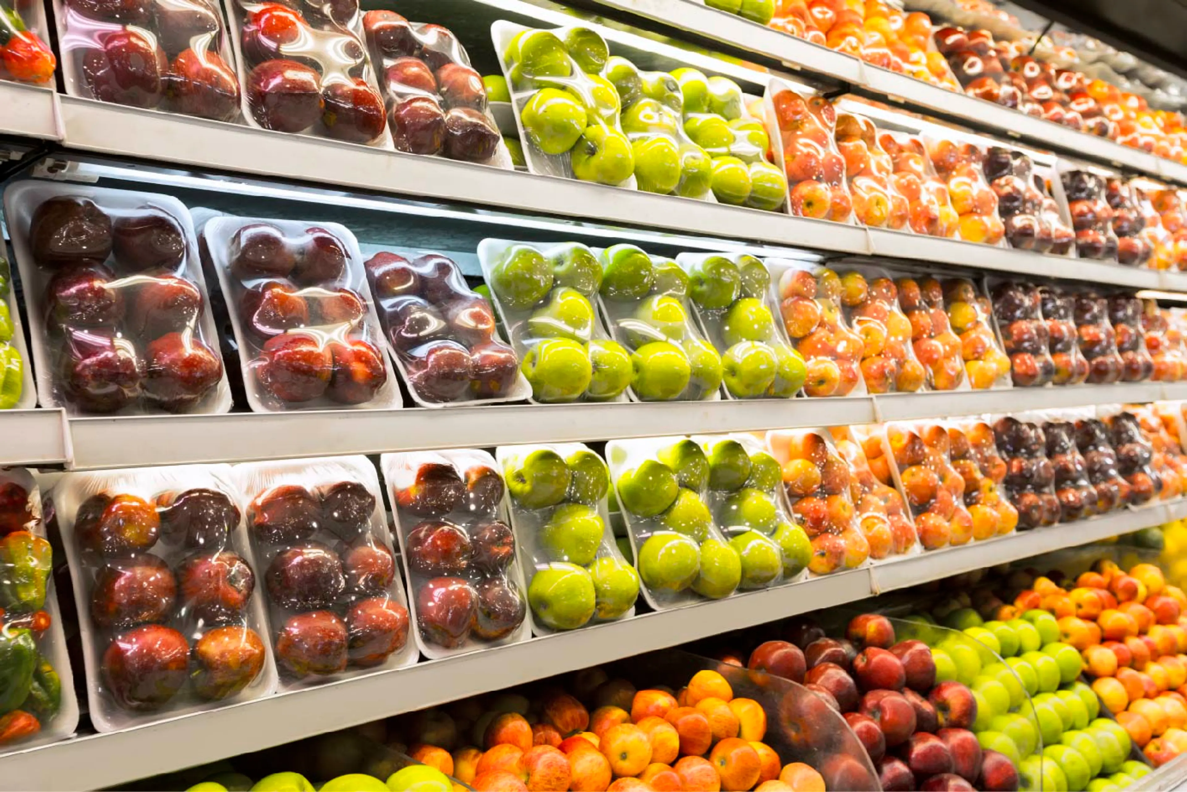 Supermarket shelf displaying fresh fruit in trays covered with food film